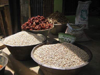 Basins of beans and dried peppers beside a sack of parboiled rice