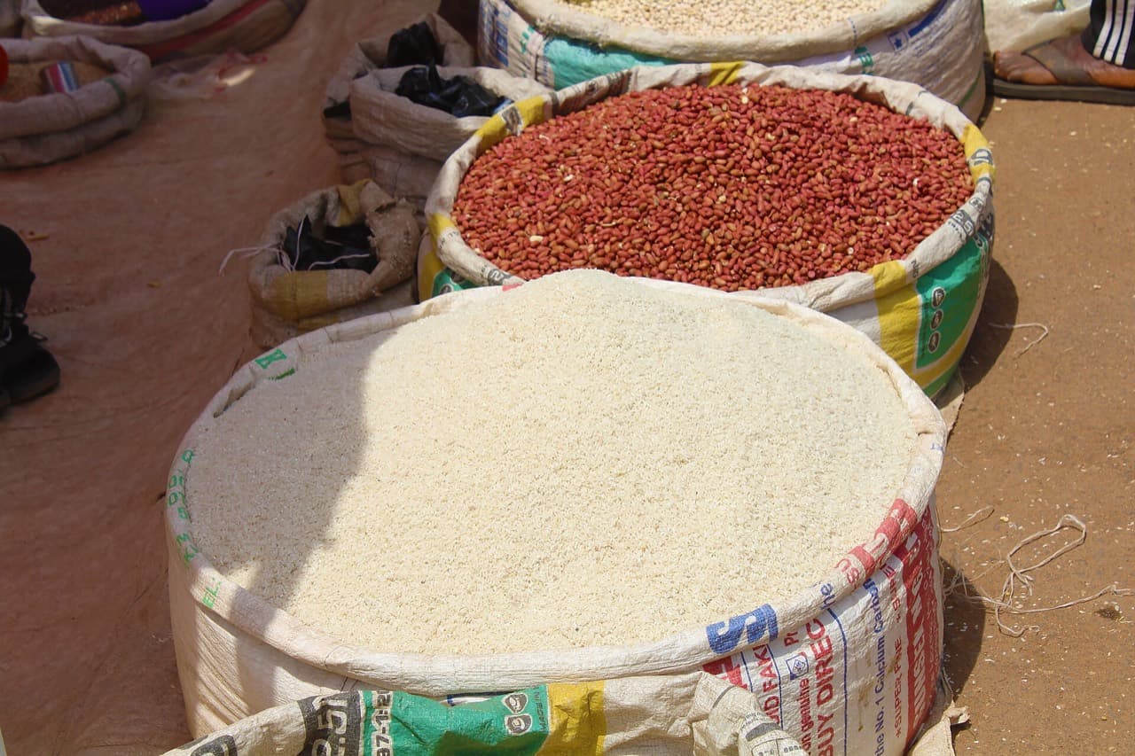 An open sack of rice beside groundnuts at a market stall